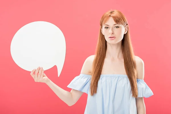 Serious attractive redhead girl holding blank speech bubble and looking at camera isolated on pink — Stock Photo