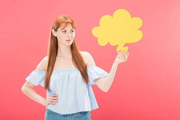 Attrayant rousse jeune femme debout avec la main sur la hanche et tenant bulle de pensée vide isolé sur rose — Photo de stock