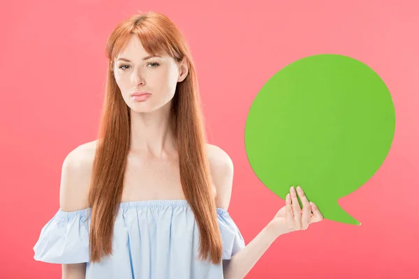 Ernsthafte attraktive rothaarige Mädchen mit grünen leeren Sprechblase und Blick in die Kamera isoliert auf rosa — Stockfoto