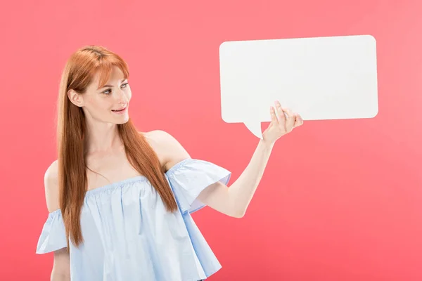 Smiling attractive redhead girl holding empty speech bubble isolated on pink — Stock Photo