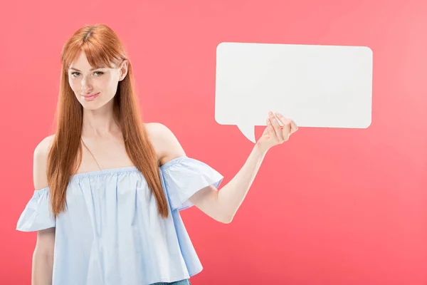 Smiling attractive redhead girl holding empty speech bubble isolated on pink — Stock Photo