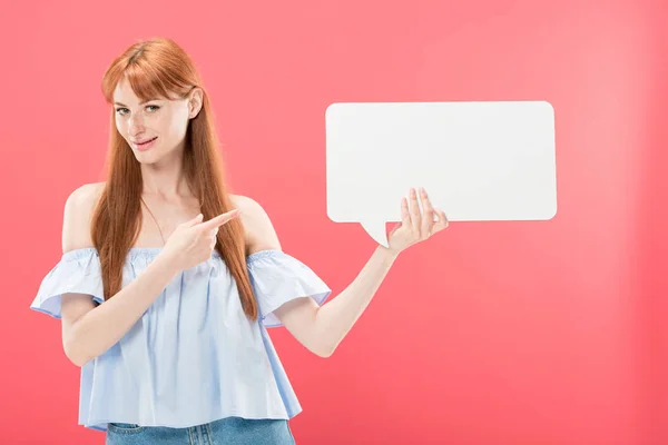 Rothaarige junge Frau zeigt mit dem Finger auf leere Sprechblase und blickt isoliert in die Kamera auf rosa — Stockfoto