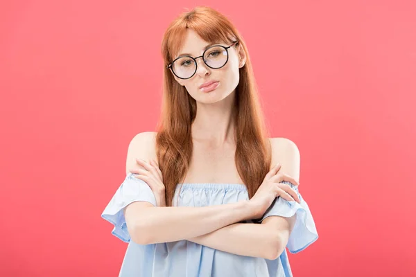 Front view of serious redhead girl in glasses standing with crossed arms and looking at camera isolated on pink — Stock Photo
