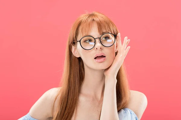 Curious redhead woman looking at camera and touching glasses isolated on pink — Stock Photo