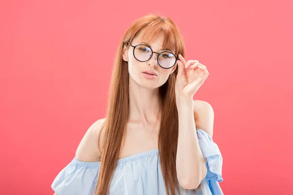 Front view of curious redhead woman looking at camera and touching glasses isolated on pink — Stock Photo