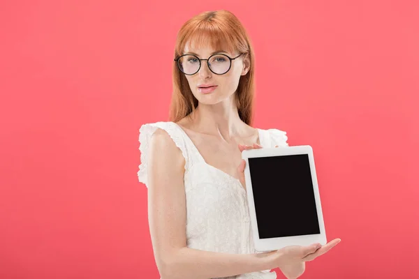 Belle rousse fille en lunettes et robe blanche tenant tablette numérique avec écran vide et regardant la caméra isolée sur rose — Photo de stock