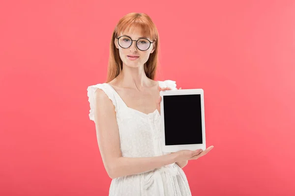 Belle rousse fille en lunettes et robe blanche tenant tablette numérique avec écran vide et regardant la caméra isolée sur rose — Photo de stock