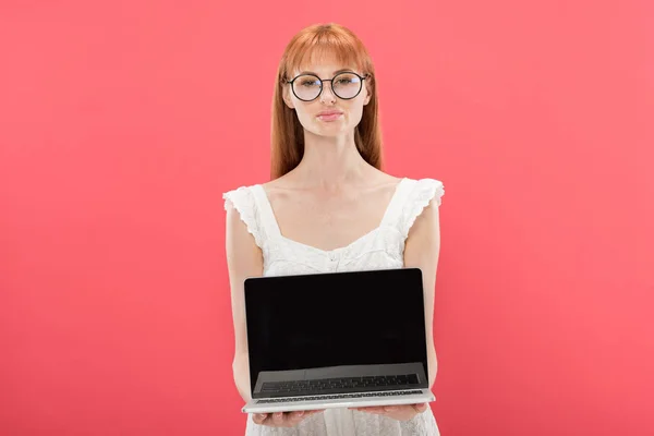 Вид спереди рыжеволосой молодой женщины в очках, держащей ноутбук с экраном, изолированным на розовом фоне — стоковое фото