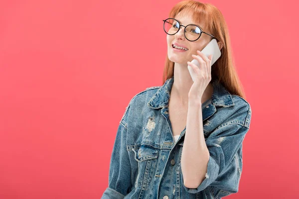 Jolie rousse fille en lunettes et veste en denim parler sur smartphone isolé sur rose — Photo de stock