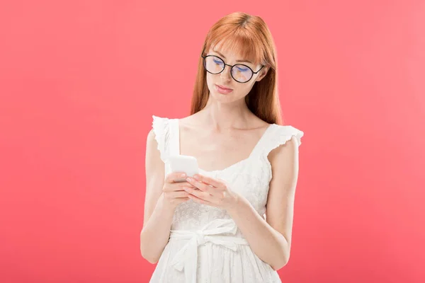 Rothaarige Frau in Brille und weißem Kleid mit Smartphone isoliert auf rosa — Stockfoto