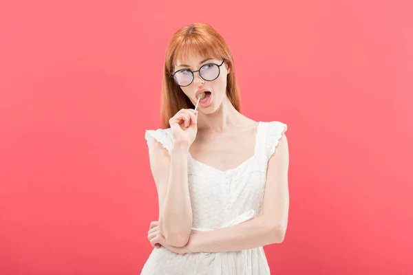 Chère fille dans lunettes manger sucette et regarder loin isolé sur rose — Photo de stock