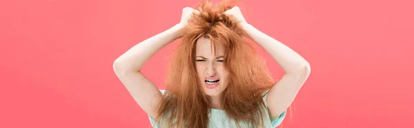 Plan panoramique de rousse en colère femme touchant les cheveux emmêlés isolé sur rose — Photo de stock