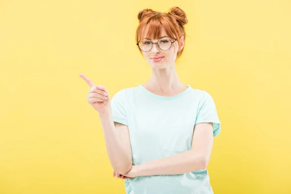 Redhead girl in glasses and t-shirt pointing with fingers isolated on yellow — Stock Photo