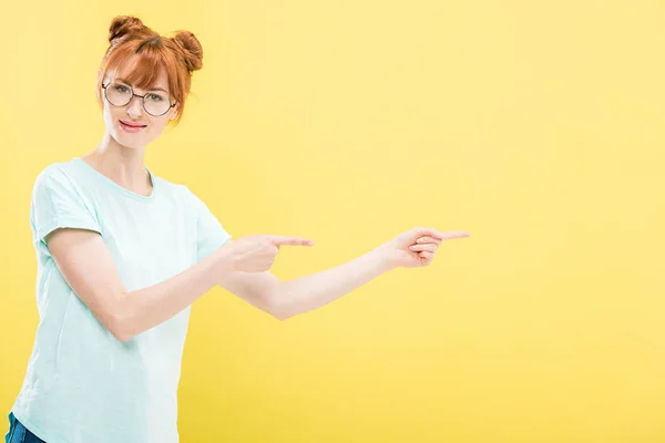 Rothaariges Mädchen mit Brille und T-Shirt, das mit den Fingern auf gelb zeigt — Stockfoto
