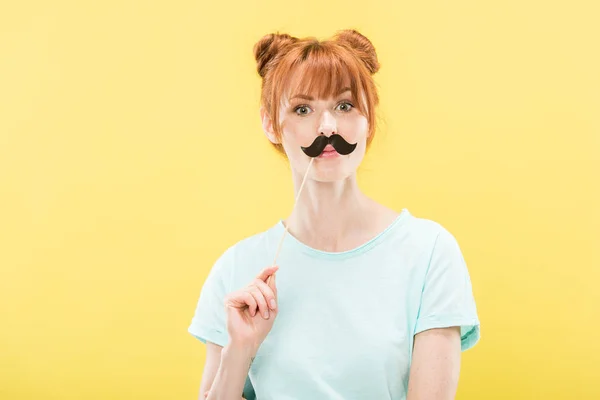 Front view of surprised redhead girl in t-shirt holding toy mustache — Stock Photo