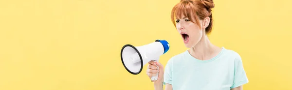 Colpo panoramico di rossa arrabbiata giovane donna che tiene il megafono e urla isolato sul giallo — Foto stock