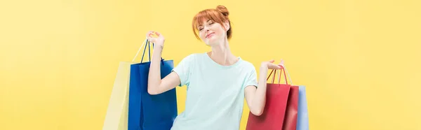 Tiro panorâmico de menina ruiva sorridente segurando saco de compras isolado no amarelo — Fotografia de Stock