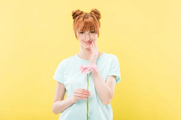 Front view of smiling redhead young woman in t-shirt holding flower and looking at camera isolated on yellow — Stock Photo