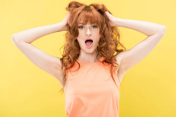 Frontansicht einer schockierten rothaarigen Frau, die Haare berührt und in die Kamera schaut, isoliert auf gelb — Stockfoto