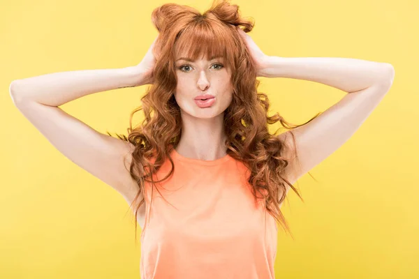 Vista frontal de chica pelirroja bonita tocando el pelo rizado y mirando a la cámara aislada en amarillo - foto de stock