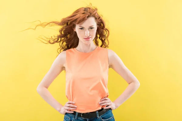 Front view of attractive redhead curly woman with hands on hips looking at camera isolated on yellow — Stock Photo