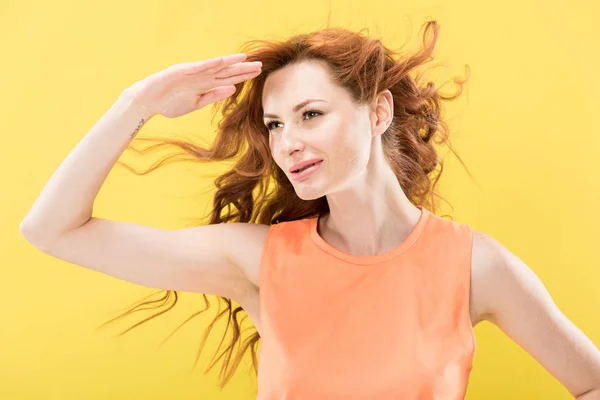 Smiling curly redhead woman looking in distance isolated on yellow — Stock Photo