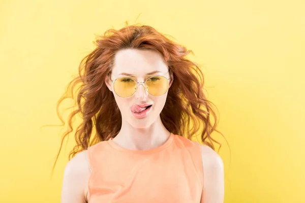 Vorderansicht der lockigen rothaarigen Frau mit Sonnenbrille leckt Lippen isoliert auf gelb — Stockfoto