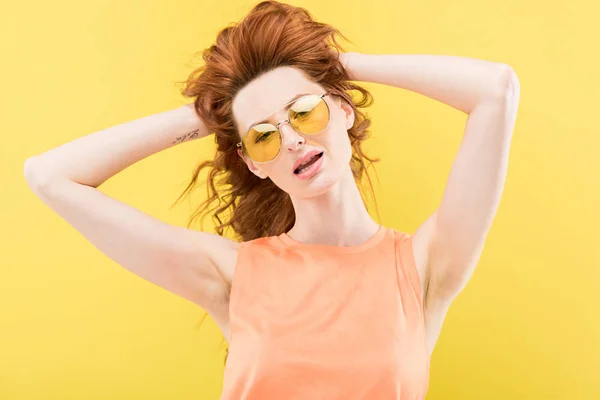 Excité rousse fille en lunettes de soleil toucher les cheveux bouclés isolé sur jaune — Photo de stock