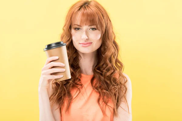Vista frontale di riccio sorridente rossa ragazza in possesso di tazza di carta di caffè isolato su giallo — Foto stock