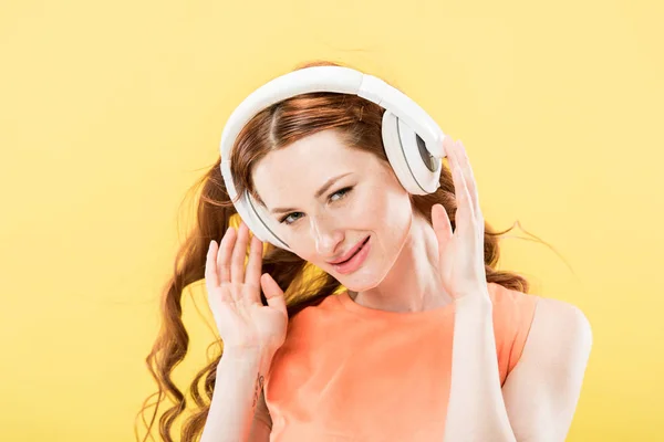 Attractive redhead woman listening music in headphones and smiling isolated on yellow — Stock Photo