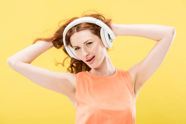 Jolie rousse femme écouter de la musique dans les écouteurs et toucher les cheveux bouclés isolé sur jaune — Photo de stock