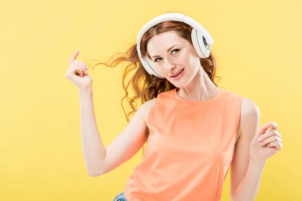 Jolie rousse femme écoute de la musique dans les écouteurs et souriant isolé sur jaune — Photo de stock