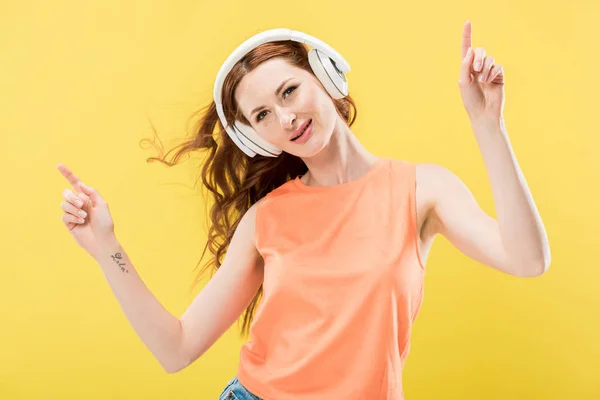Jolie rousse souriante femme écoutant de la musique dans les écouteurs et dansant isolé sur jaune — Photo de stock