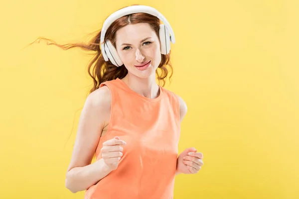 Vue de face de jolie rousse femme écoutant de la musique dans les écouteurs et souriant isolé sur jaune — Photo de stock