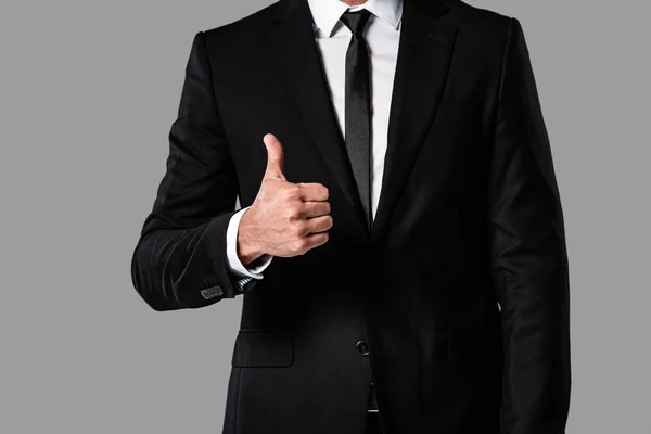 Vista ritagliata di uomo d'affari in abito nero mostrando pollice in su isolato sul grigio — Foto stock