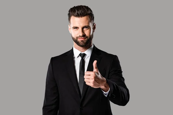 Smiling handsome businessman in black suit showing thumb up isolated on grey — Stock Photo