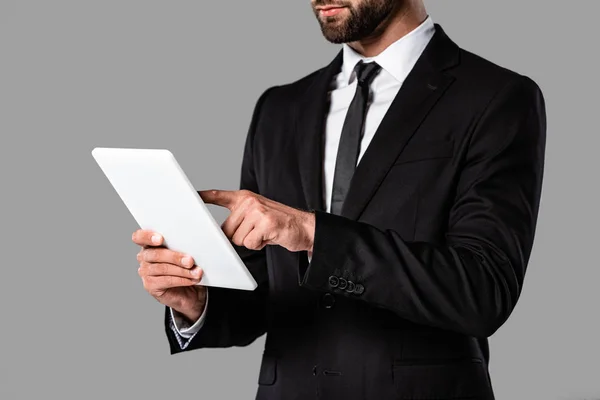 Vista parcial del hombre de negocios en traje negro usando tableta digital aislada en gris - foto de stock