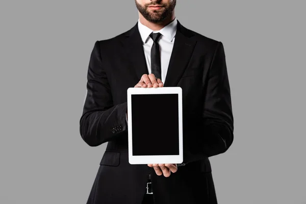 Vista parcial del hombre de negocios en traje negro mostrando tableta digital con pantalla en blanco aislada en gris - foto de stock