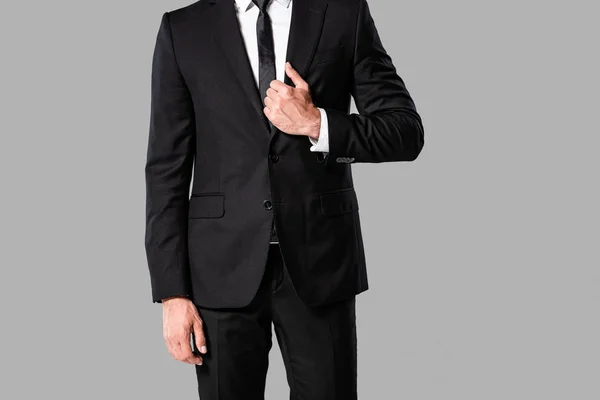 Частичный взгляд элегантного бизнесмена в черном костюме и галстуке, изолированном на сером — стоковое фото