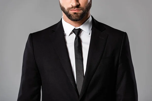 Обрезанный вид серьезного бородатого бизнесмена в черном костюме, изолированного на сером — стоковое фото