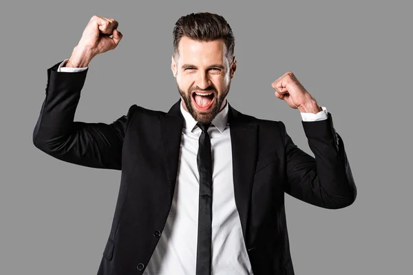 Feliz hombre de negocios en traje negro mostrando sí gesto aislado en gris - foto de stock