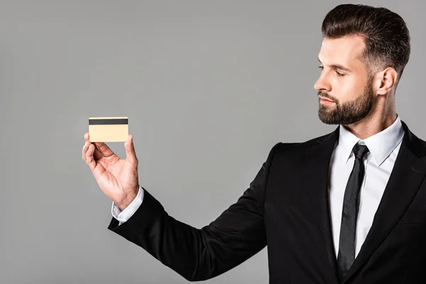 Schöner Geschäftsmann im schwarzen Anzug mit Kreditkarte isoliert auf grau — Stockfoto