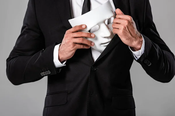 Partial view of businessman in black suit holding white mask isolated on grey — Stock Photo