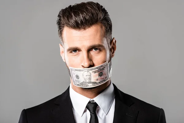 Uomo d'affari in completo nero con banconota da un dollaro in bocca isolato su grigio — Stock Photo