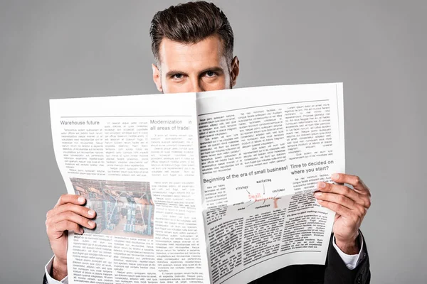 Confident businessman in black suit with newspaper isolated on grey — Stock Photo