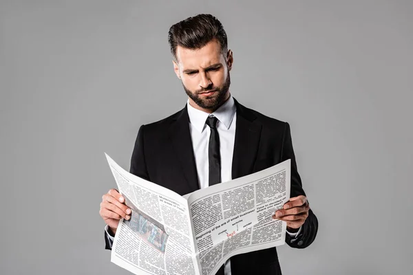 Серйозний бізнесмен в чорному костюмі читає газету ізольовано на сірому — стокове фото
