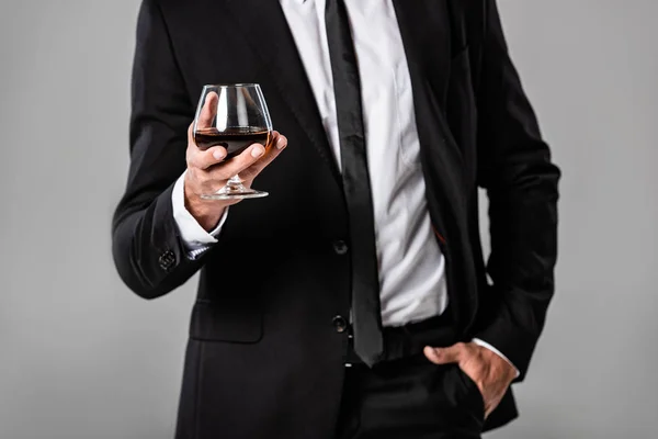 Cropped view of businessman in black suit holding glass with whiskey isolated on grey — Stock Photo