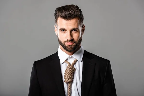 Hombre de negocios guapo deprimido en traje negro con soga en el cuello aislado en gris - foto de stock