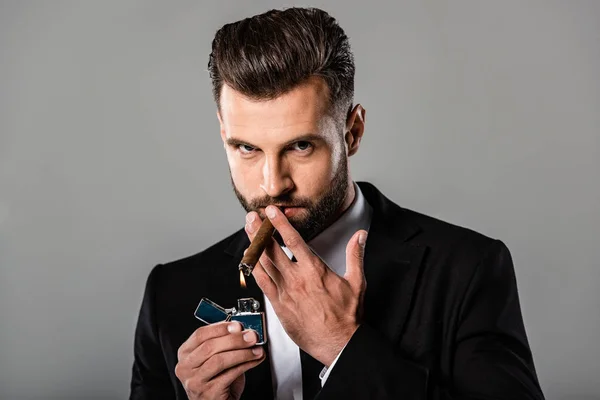 Businessman in black suit lighting up cigar isolated on grey — Stock Photo