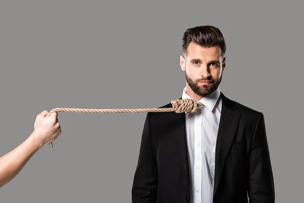 Depressed businessman in black suit with noose on neck near murderer with rope isolated on grey — Stock Photo